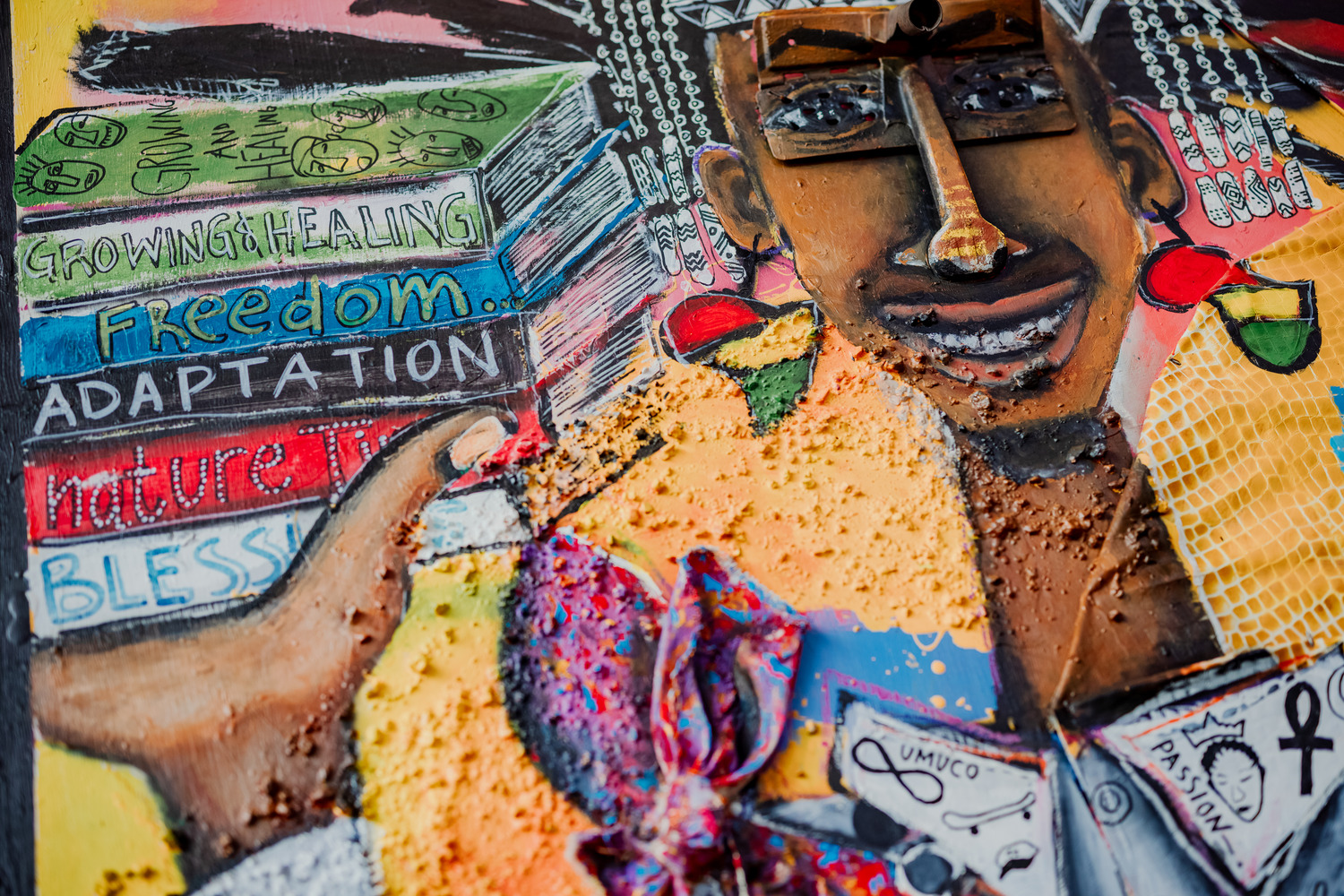 Colorful mural by a San Antonio artist depicts a person wearing glasses, holding books labeled with themes like healing and adaptation, surrounded by artistic symbols that celebrate storytelling and creativity.